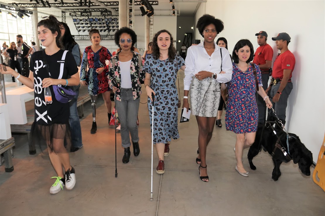 oito mulheres, com e sem deficiência, saindo da sala do desfile.